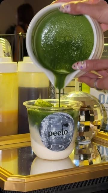 Fresh green matcha being poured into a Peelo cup over milk and ice